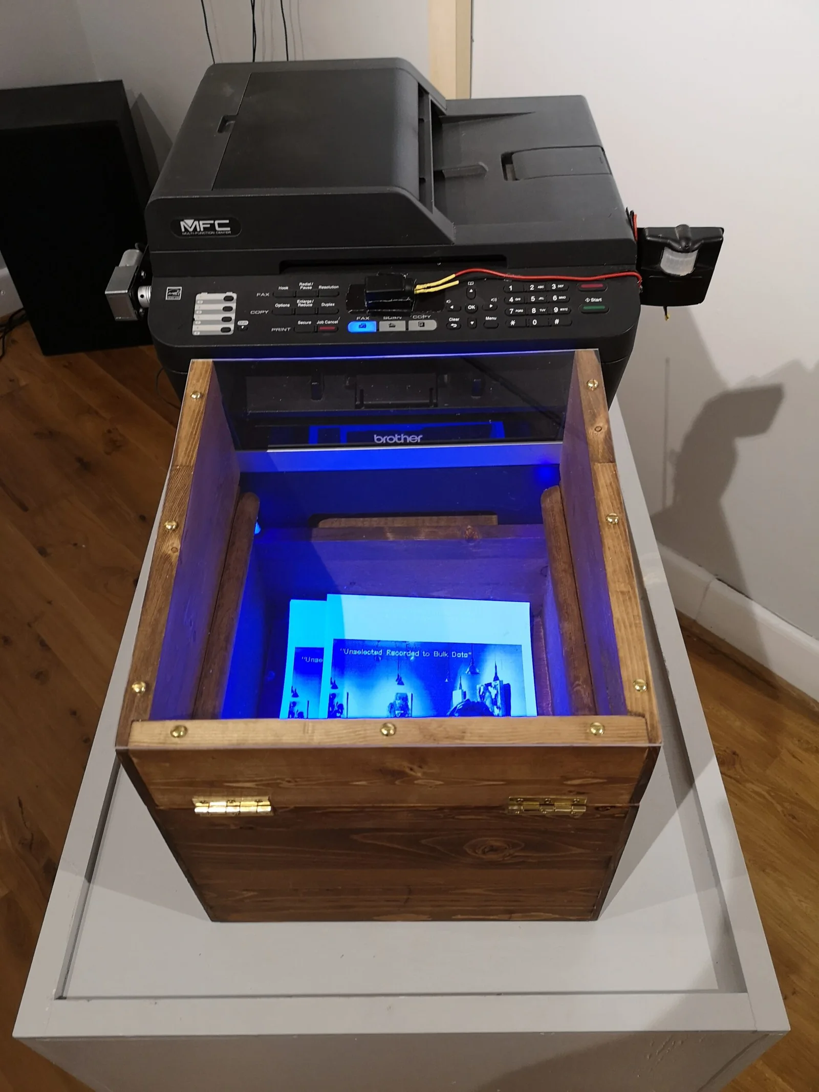 Printer and locked wooden box containing blue-lit printed records