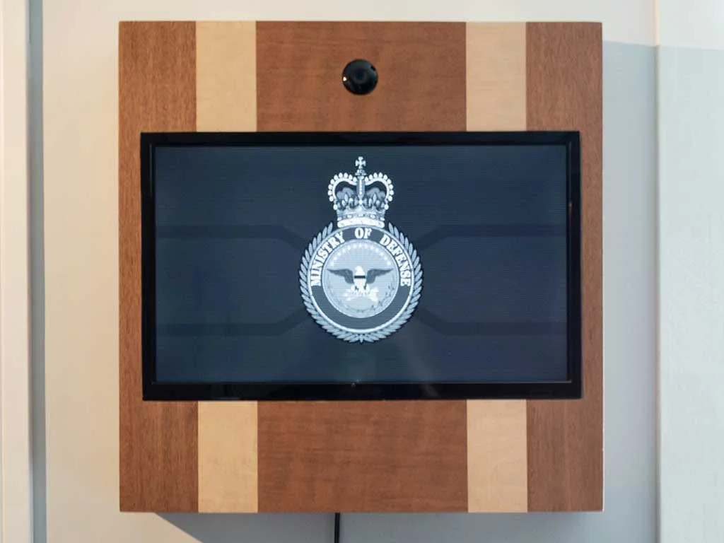 Wooden wall-mounted screen with a camera above it displaying an institutional emblem