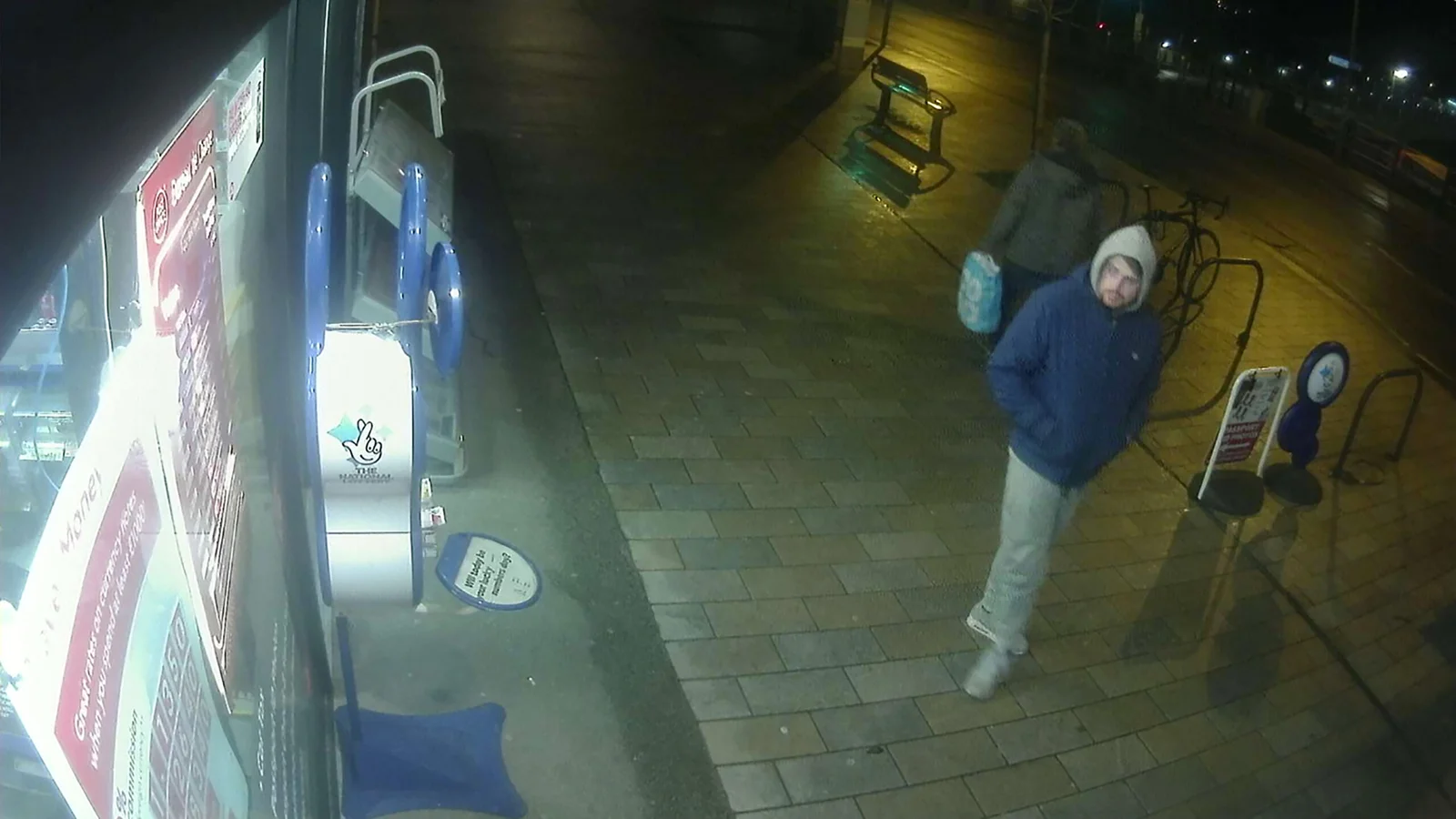 Two pedestrians walking past a storefront at night