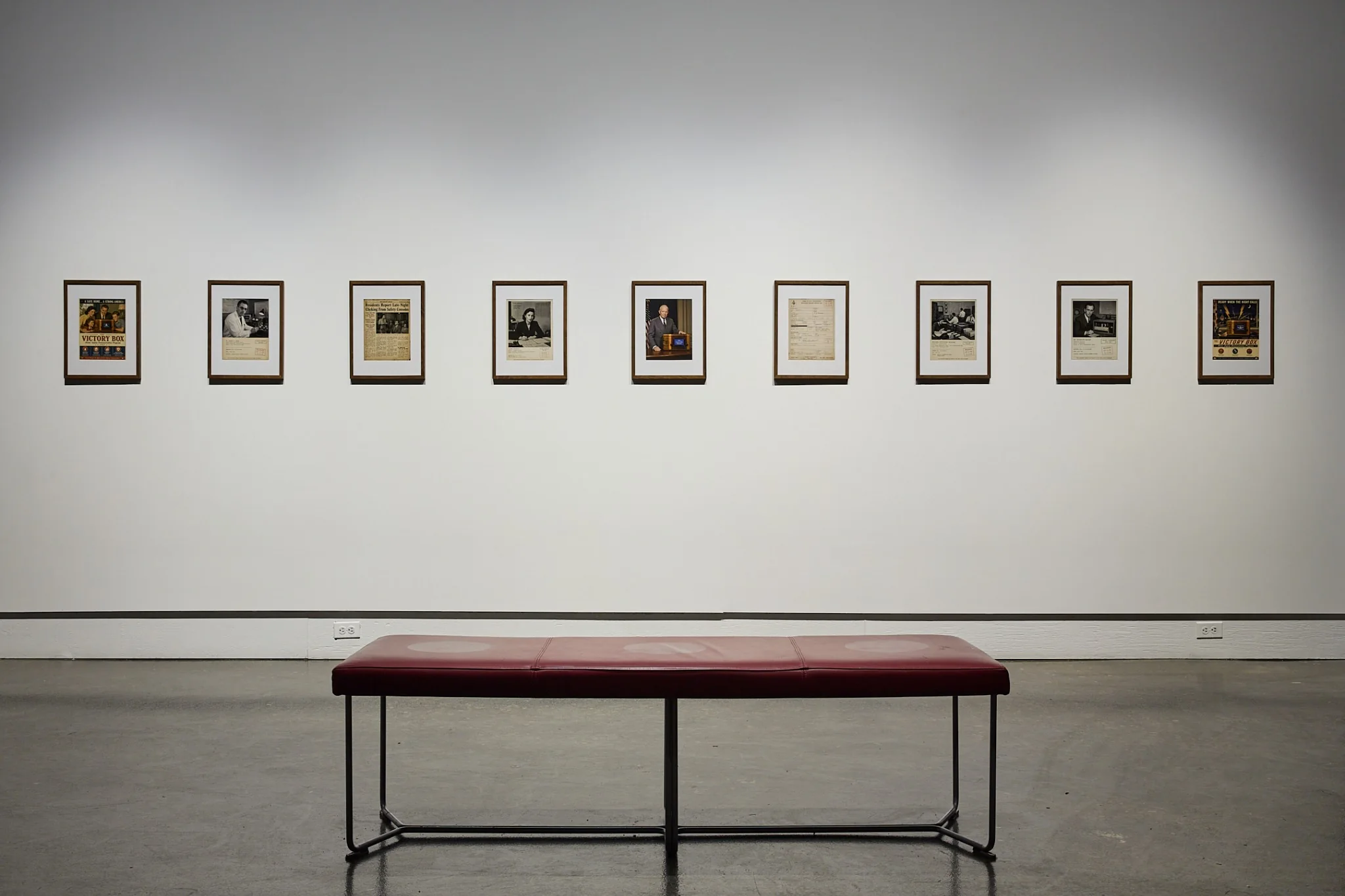 Nine framed fictional archival photographs and documents arranged across a gallery wall