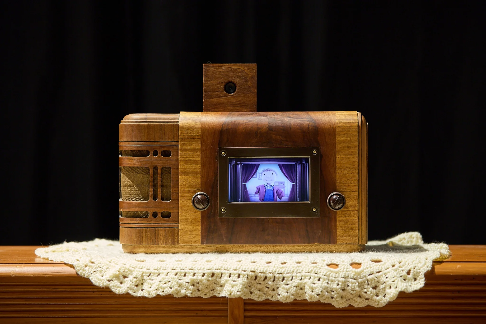 Front view of the wooden Victory Box showing a puppet program on its small screen and a camera above
